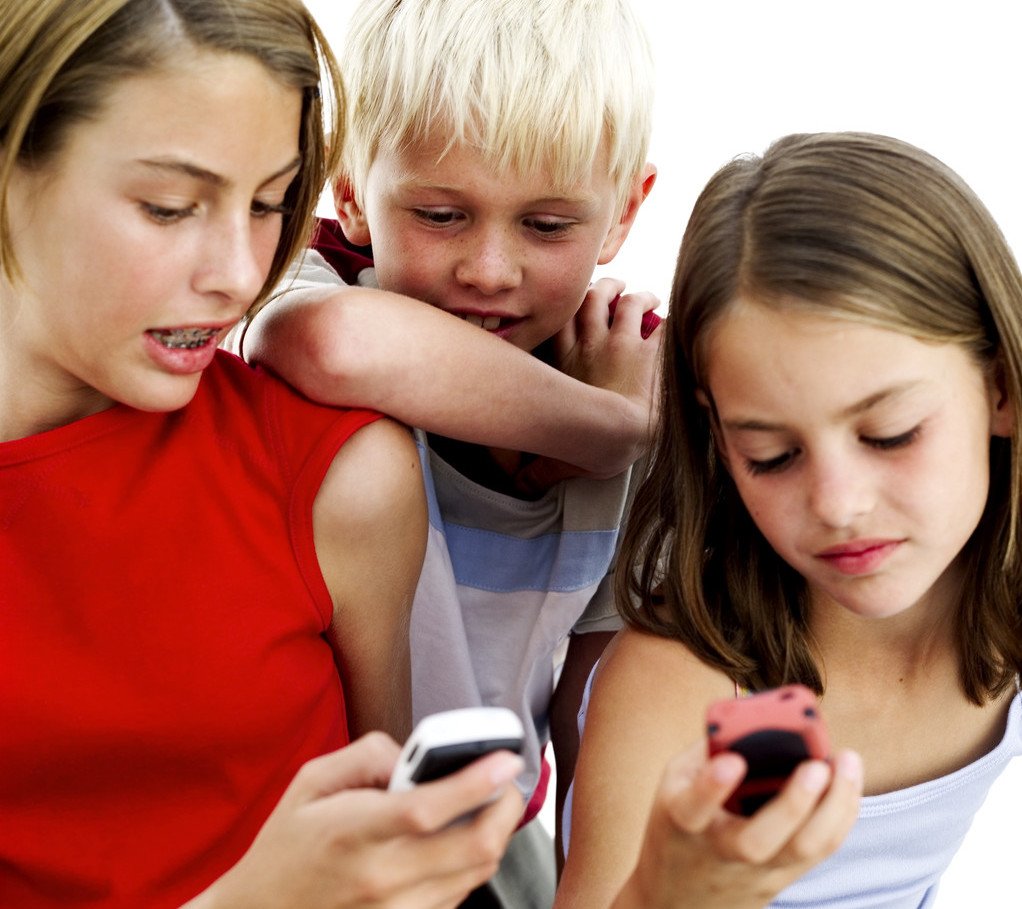 Young Girls Operating Cell Phones with a Young Boy (10-14) Standing Behind Them
